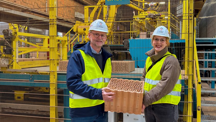 Vera Leibold, Deutschlandstipendiatin der Frankfurt University of Applied Sciences, gemeinsam mit Dipl.-Ing. Rudolf Bax beim Besuch des Hörl+Hartmann Werks in Hainburg. Beide halten einen Ziegelstein in der Produktion des Werks in den Händen.